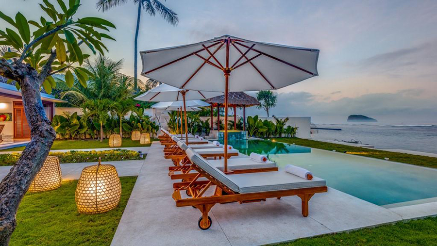 Villa Oceana's pool and pavilions lit up at twilight, palm trees silhouetted behind