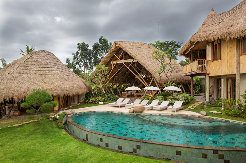 Villa Omah Padi's lagoon-style pool ringed by thatched bamboo eco-pavilions and lawn near Ubud