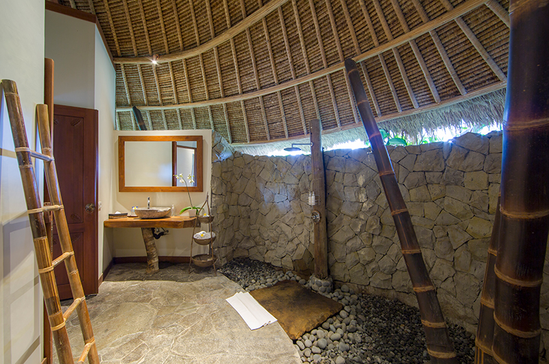 Open-air stone bathroom at Villa Omah Padi with a rain shower and a domed thatched ceiling