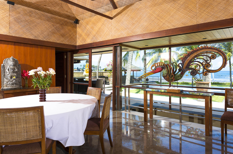 Open dining pavilion at Villa Pushpapuri looking out through glass walls to the garden, a Balinese bird carving and the ocean beyond