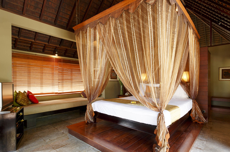 Bedroom at Villa Pushpapuri with a four-poster bed draped in gold gauze under a thatched ceiling