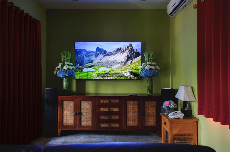 Bedroom at Villa Pushpapuri with olive walls, rattan cabinetry and floral arrangements