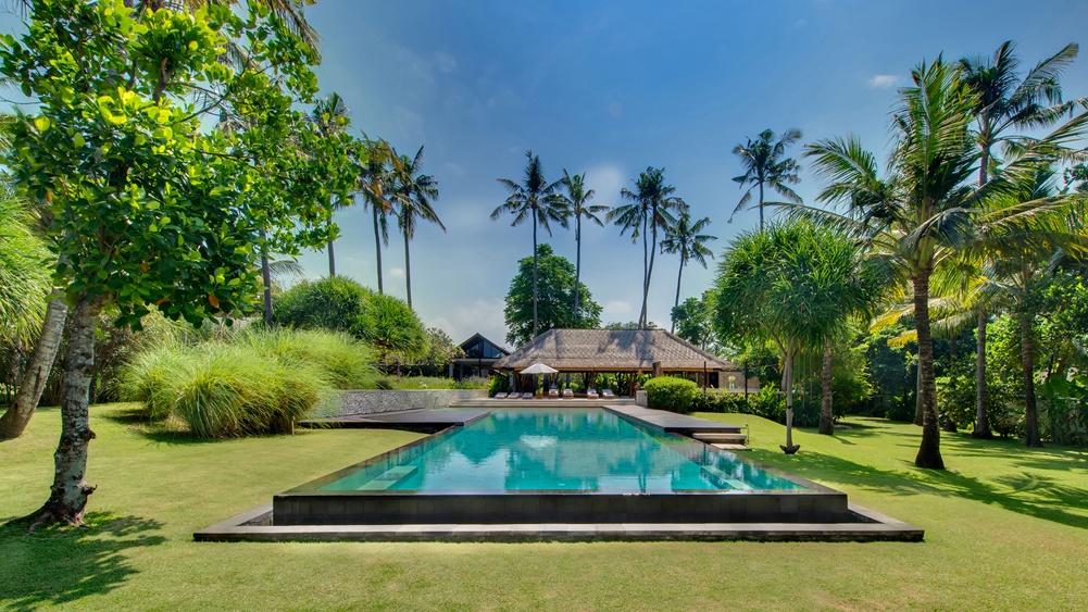 The swimming pool at Villa Samadhana set in the lawn, framed by tall coconut palms with a garden pavilion behind