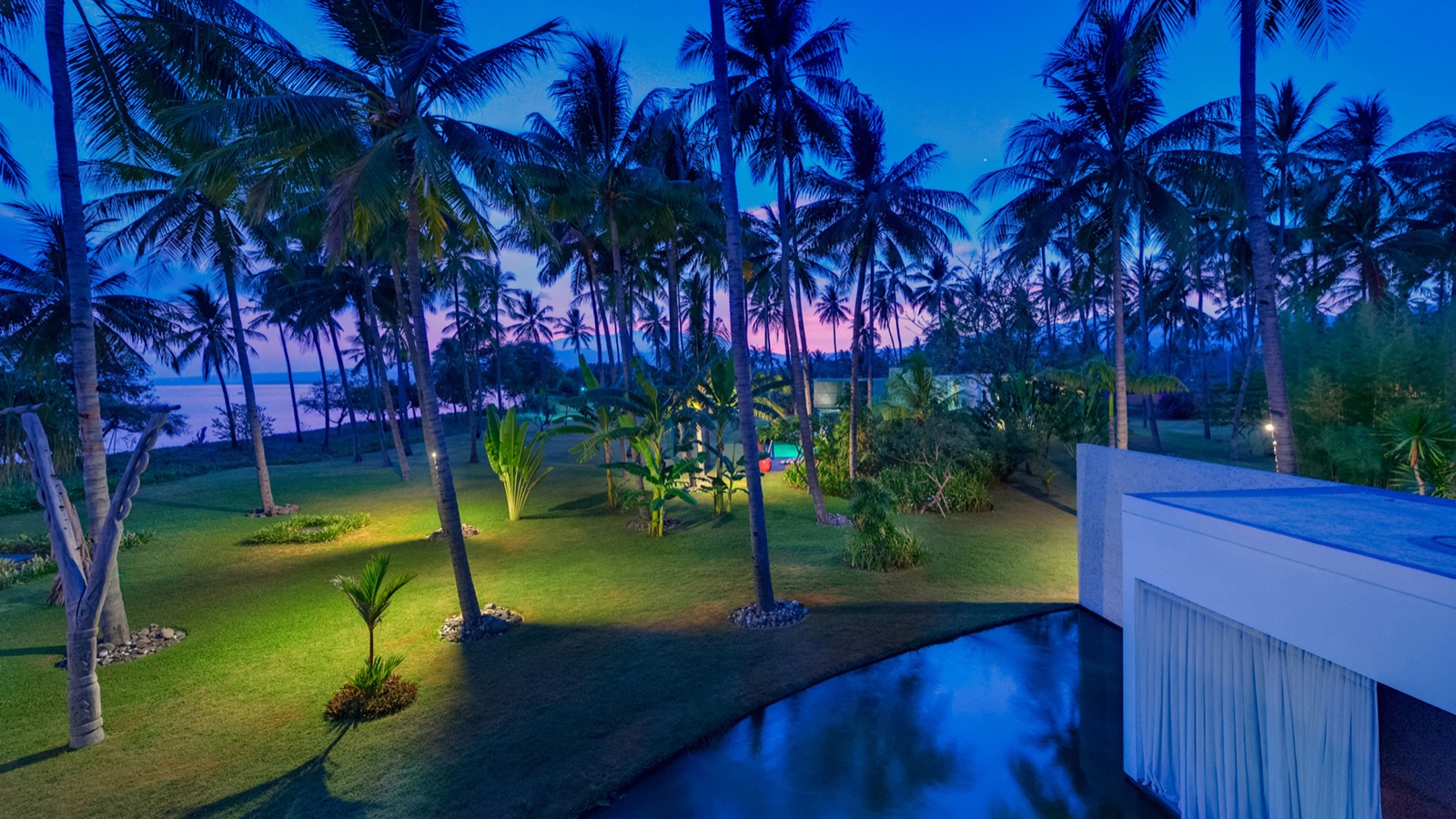 Lit lawns and water features at dusk looking toward the sea at Villa Sapi on Lombok's northwest coast