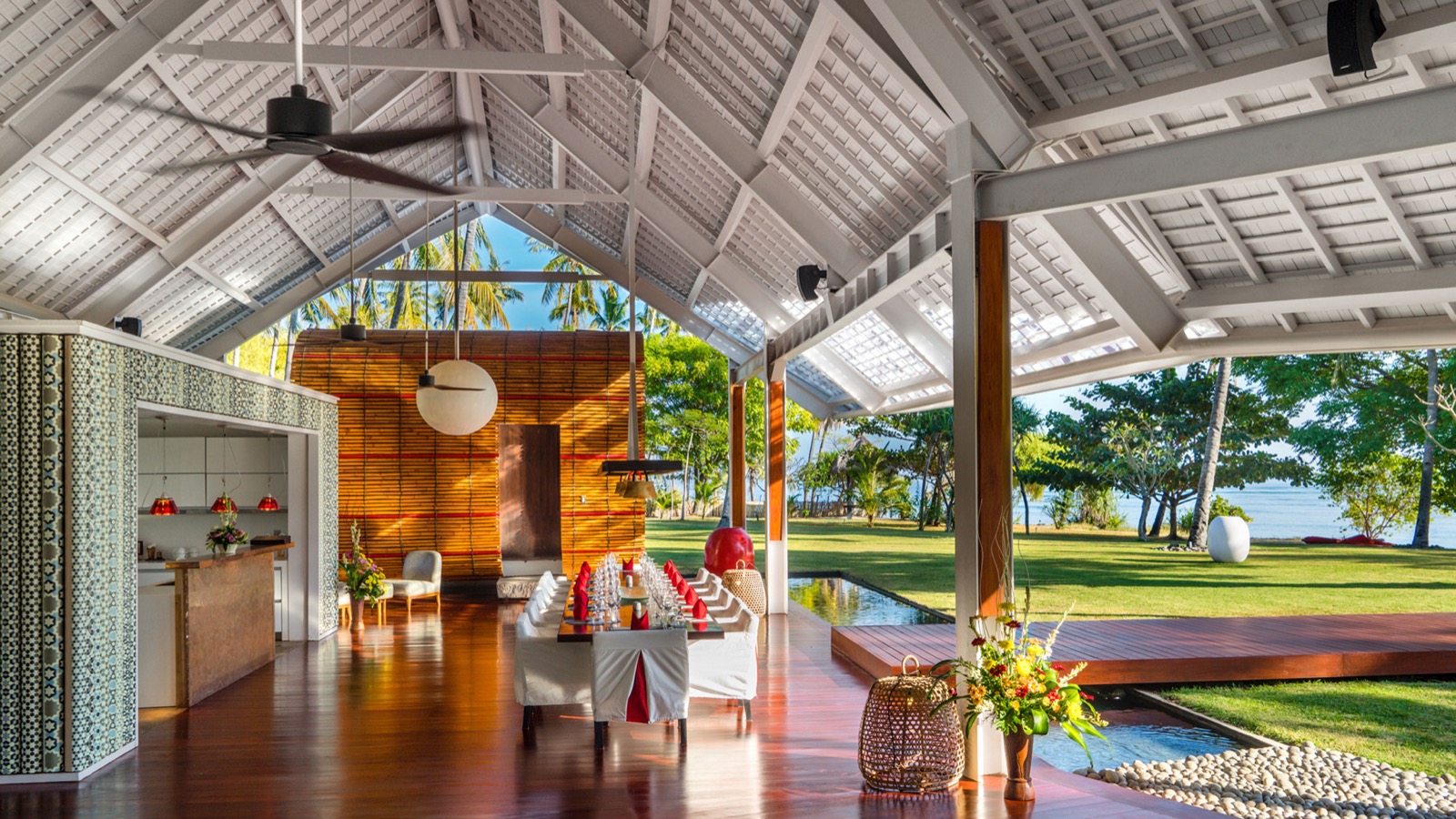 The open-sided living and dining pavilion at Villa Sapi set for a long lunch with the lawn and sea beyond