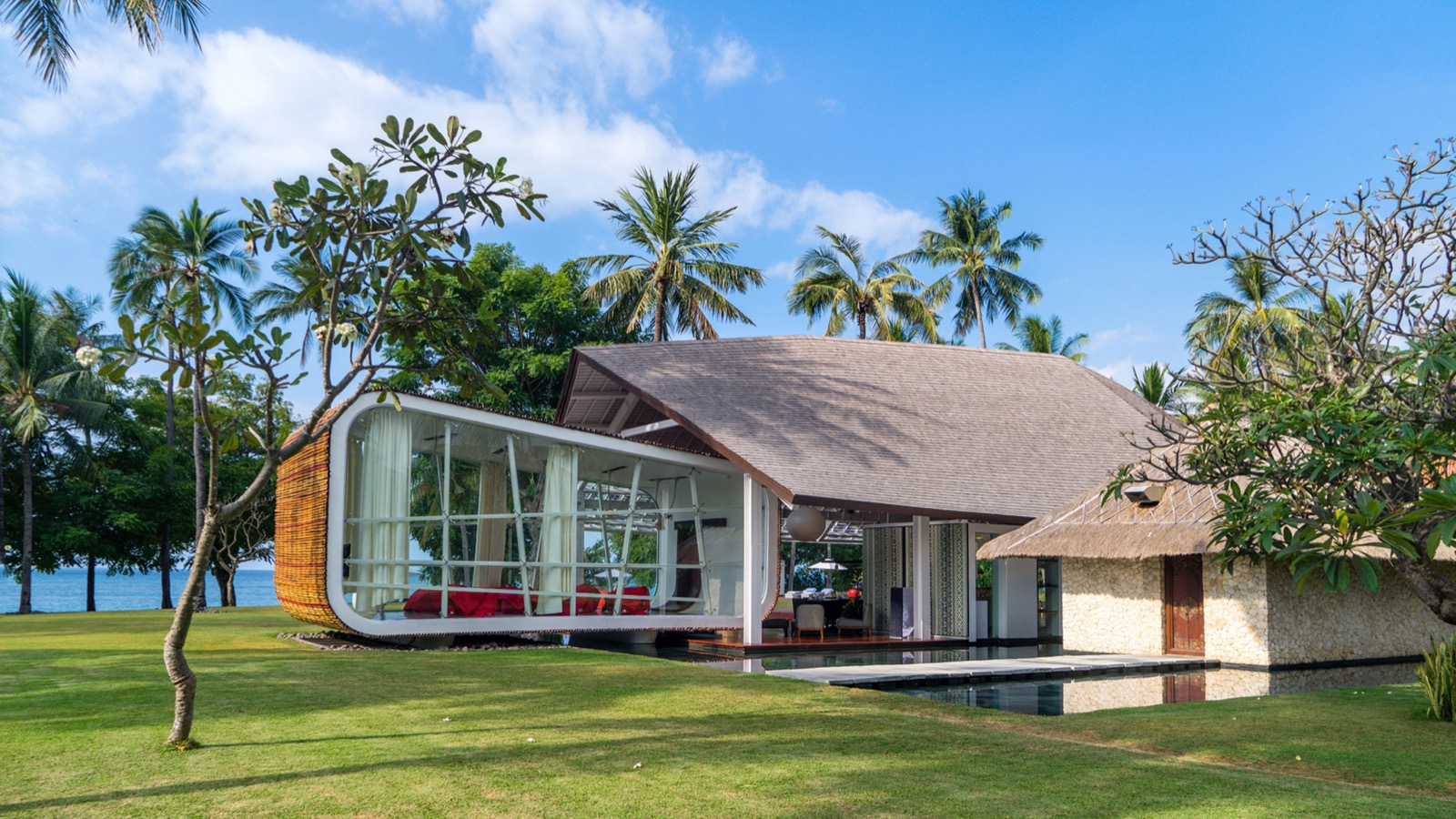 The curved glass pavilion of Villa Sapi under its shingle roof with the lawn running to the sea at Sira Beach, Lombok
