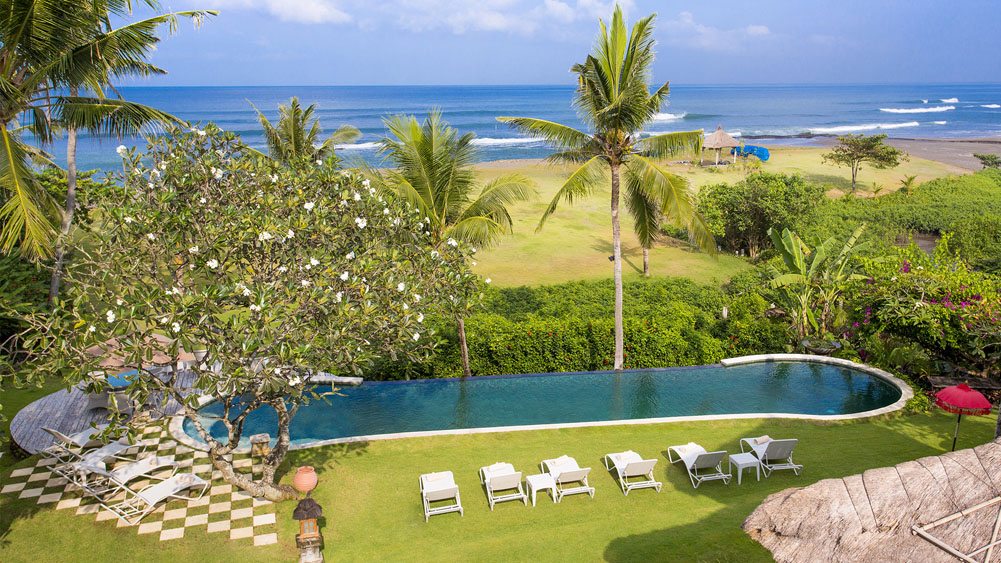 Infinity pool at Villa Sungai Tinggi with the garden lawn running down to the beach and the sea beyond