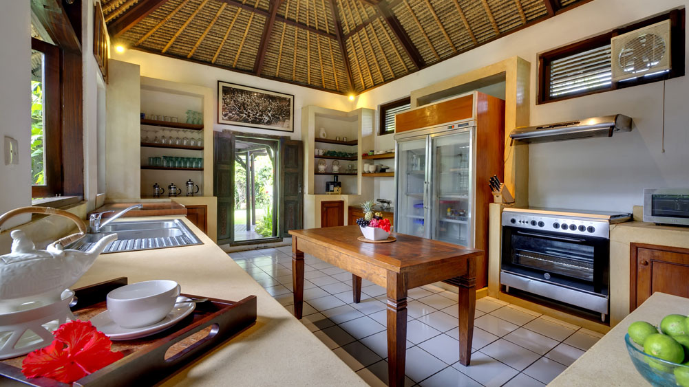 Open thatched-roof kitchen at Villa Sungai Tinggi with a teak island and range