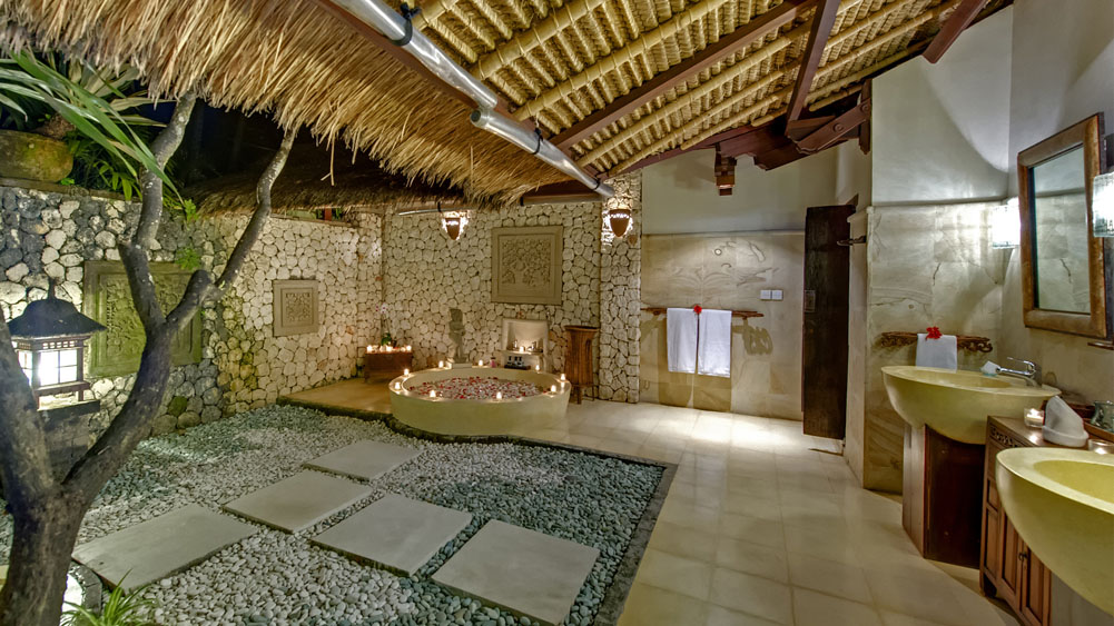 Open-air stone bathroom at Villa Sungai Tinggi with a candlelit soaking tub under a thatched roof