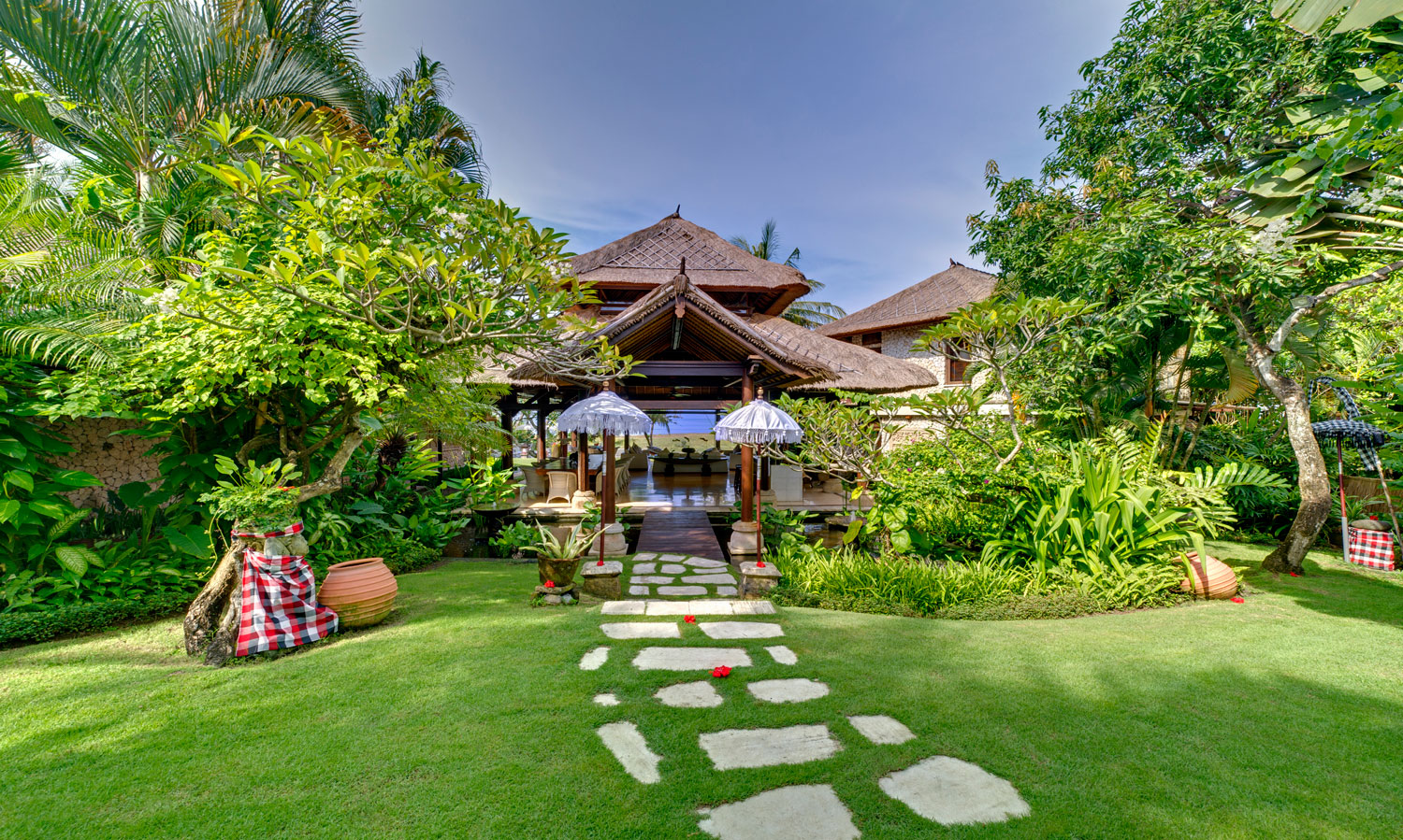 Thatched-roof pavilions of Villa Sungai Tinggi seen across the garden lawn, with a stone path leading to the open living pavilion in Canggu, Bali