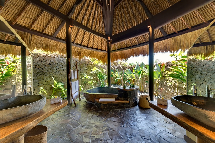 An open-air stone bathtub and shower at Villa Taman Ahimsa, set among garden stone walls