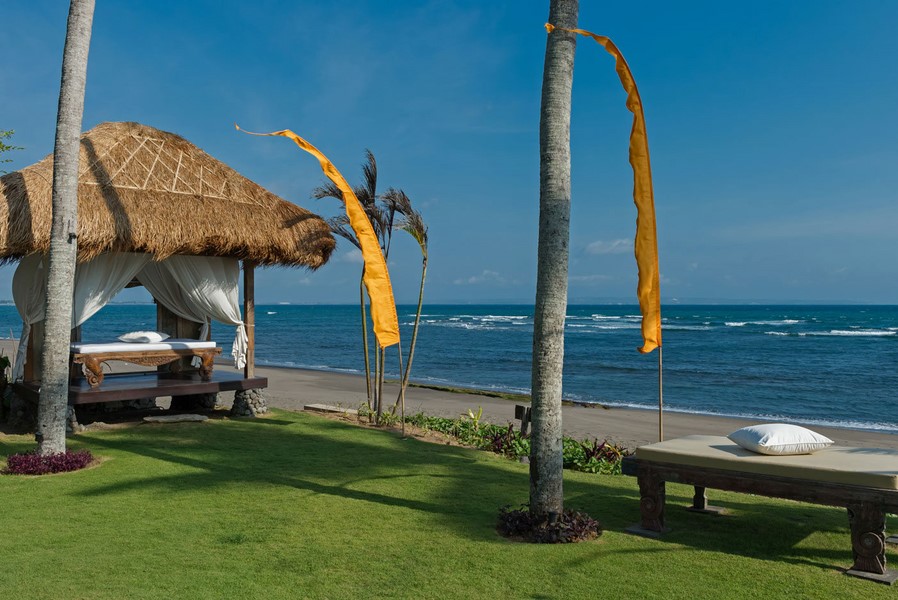 Thatched daybeds and ceremonial flags on the lawn between Villa Taman Ahimsa and the beach