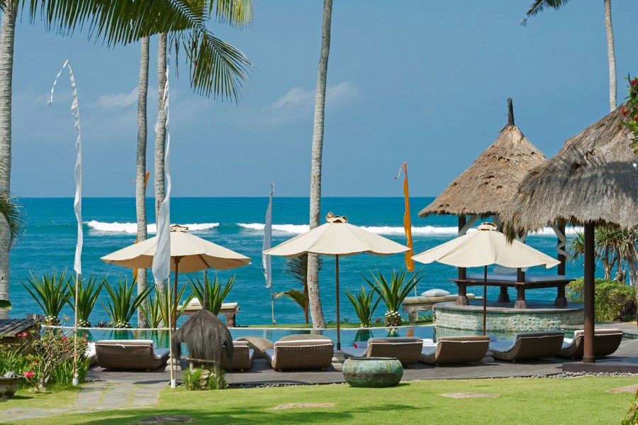 Villa Taman Ahimsa's pool deck with loungers and umbrellas facing the ocean