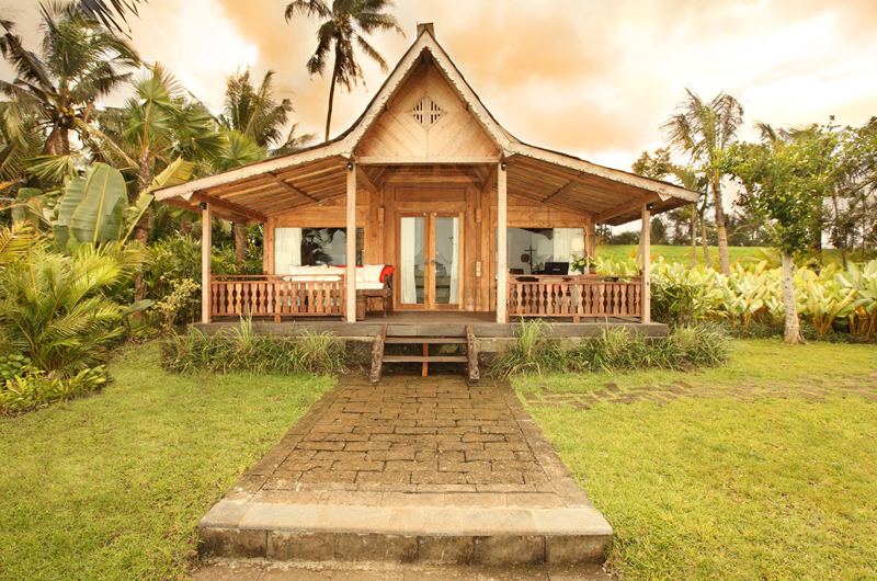A standalone teakwood bedroom pavilion set in the garden at Villa Tangguntiti at dusk