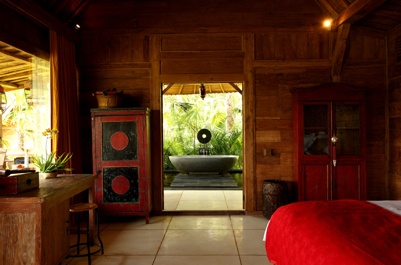 A teakwood bedroom at Villa Tangguntiti opening onto a stone garden bathtub